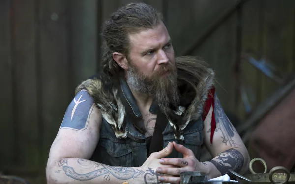 HD wallpaper of a character from Outlander, featuring a bearded man with tattoos wearing a vest with fur accents, contemplating thoughtfully.