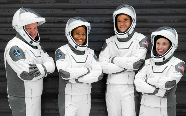 HD wallpaper featuring the Inspiration4 crew in white space suits with mission patches, smiling and posing together for a group photo.