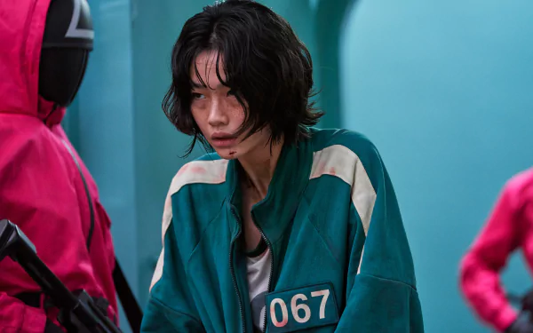 HD PC desktop wallpaper featuring Kang Sae-byeok from the TV show Squid Game, dressed in a green tracksuit with the number 067, surrounded by guards in red suits.