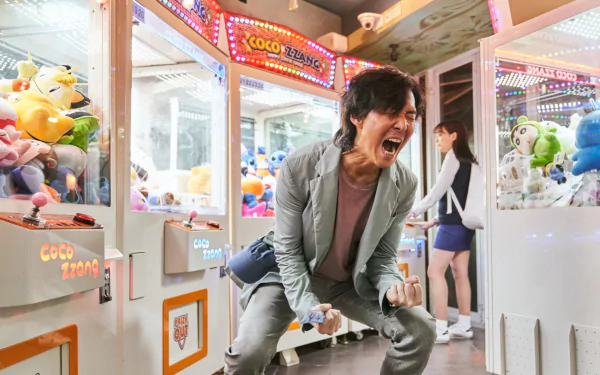 Seong Gi-Hun from the TV show Squid Game passionately plays claw machines in a vibrant arcade, captured in an HD desktop wallpaper background.