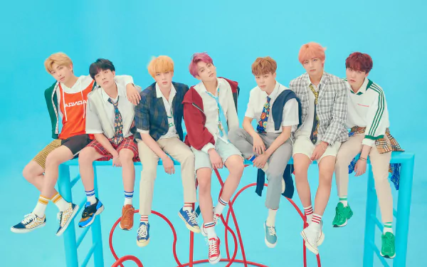 4K Ultra HD PC wallpaper showing seven young men in colorful casual outfits seated on tall stools against a bright teal backdrop with red cords, music group portrait.