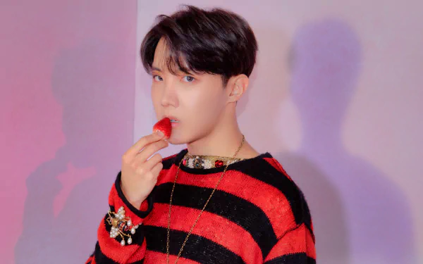 J-Hope of BTS, a K-pop singer, is captured in this vibrant 4K Ultra HD wallpaper, wearing a red and black striped sweater while holding a red object near his lips.