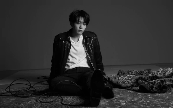 Black and white 4K Ultra HD image of Jungkook, BTS singer, sitting on the floor with music cables, capturing a moody K-pop music vibe.