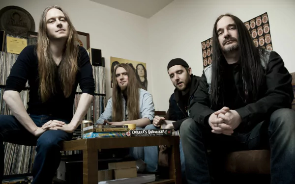 A HD desktop wallpaper featuring the band Carcass, showcasing four members casually seated in a room filled with vinyl records and eclectic decor.