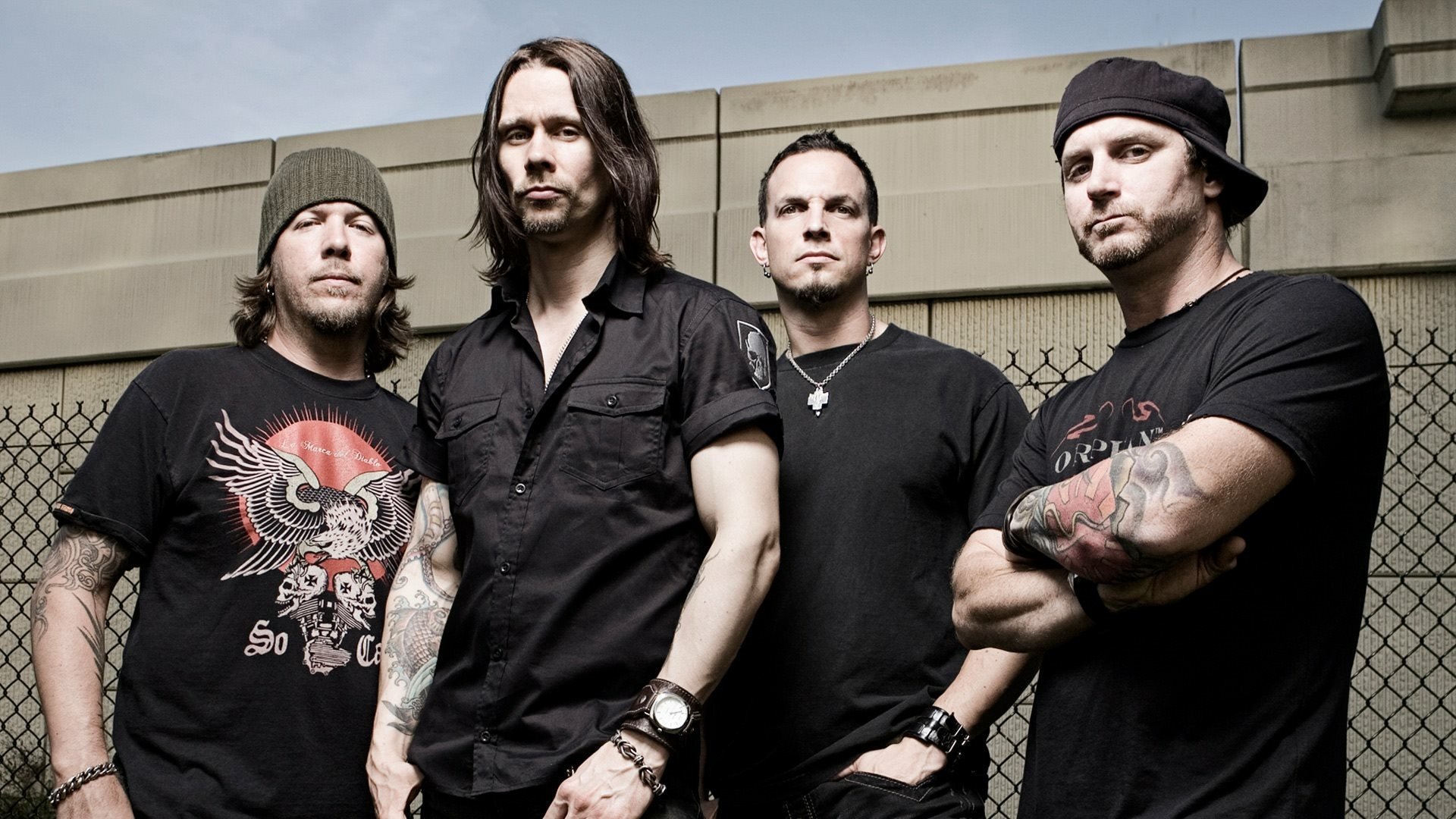 HD wallpaper featuring the band Tremonti, showcasing the four members posing confidently in a gritty outdoor setting with a chain-link fence in the background.