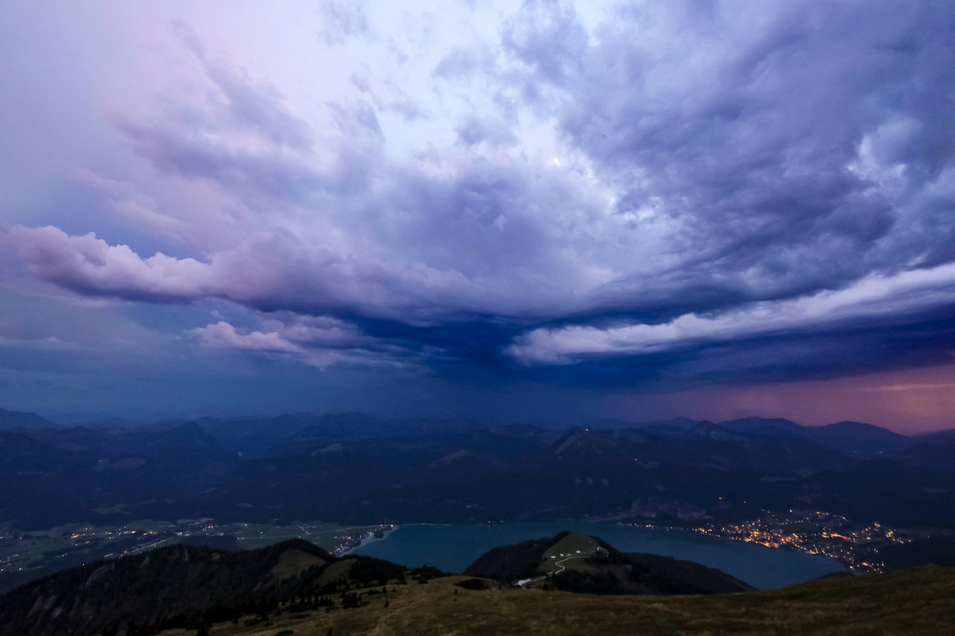 Dramatic storm clouds gather over a serene valley and lake in Austria, captured in stunning 4K Ultra HD detail for a PC desktop wallpaper.