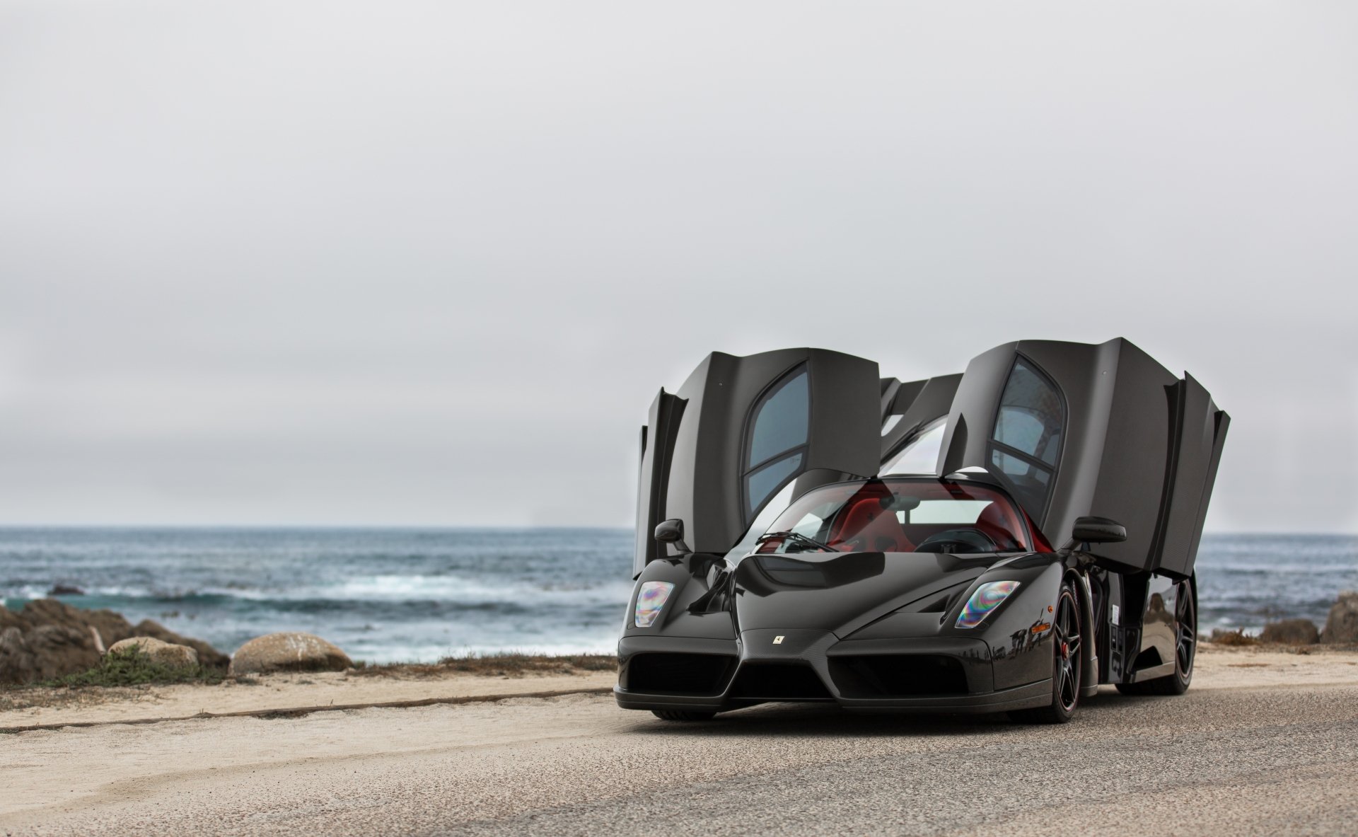 A sleek Ferrari Enzo supercar with its butterfly doors open, set against a coastal backdrop, captured in 4K Ultra HD for a stunning PC desktop wallpaper.