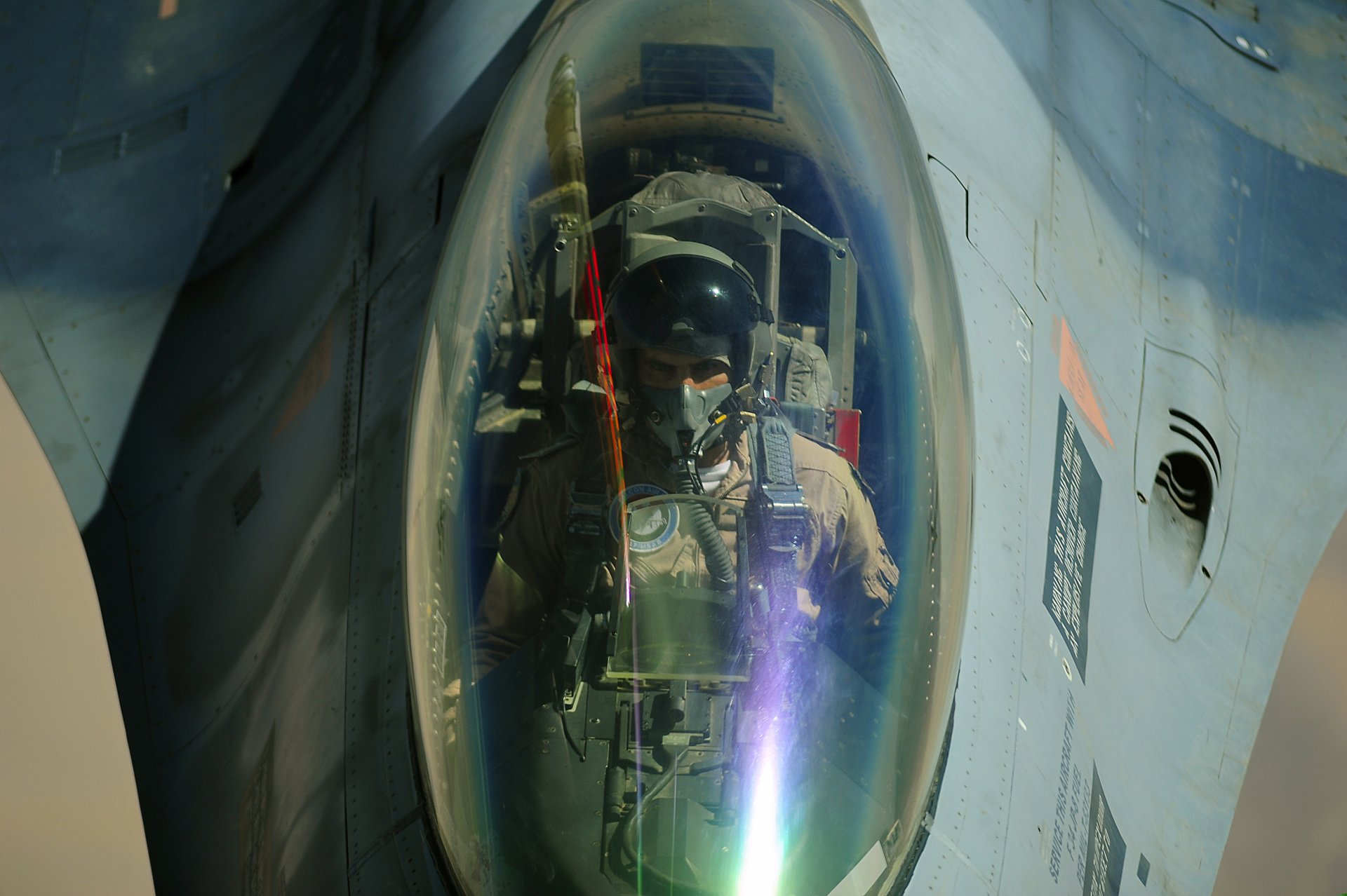 Close-up 4K Ultra HD image of a pilot in the cockpit of a General Dynamics F-16 Fighting Falcon military jet, showcasing intricate cockpit details and reflections.