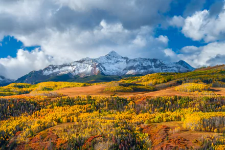 5K Ultra HD PC desktop wallpaper: fall mountain nature landscape with golden aspen meadows, rolling hills and a snow-capped peak under dramatic clouds.