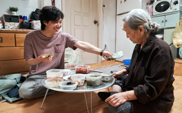 Lee Jung-jae shares a moment with an elderly woman over a meal in a scene from the TV show Squid Game, captured in 4K Ultra HD quality for PC desktop wallpaper.