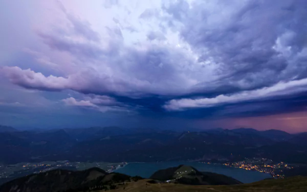 Dramatic storm clouds gather over a serene valley and lake in Austria, captured in stunning 4K Ultra HD detail for a PC desktop wallpaper.