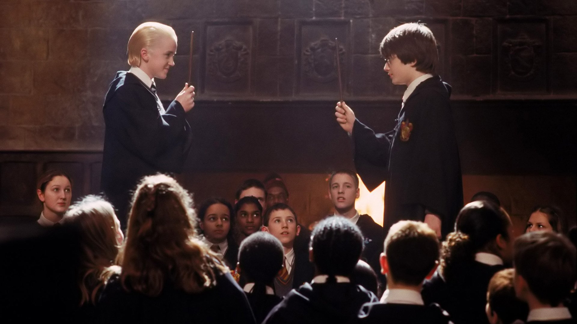 Daniel Radcliffe as Harry Potter and Tom Felton as Draco Malfoy face off in a scene from Harry Potter and the Chamber of Secrets with students watching in the Great Hall.