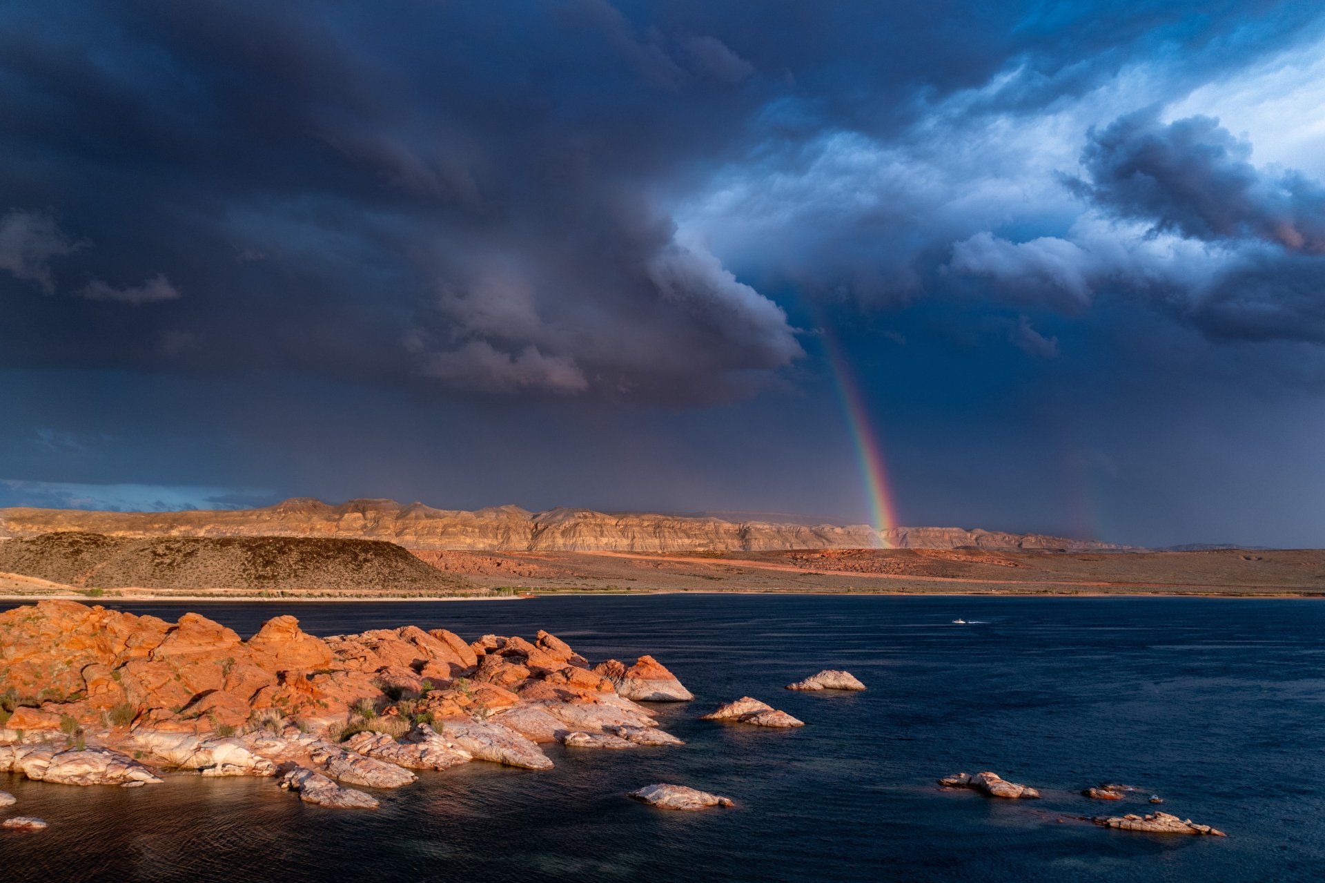 A vibrant rainbow arcs over a rugged rocky shoreline under stormy clouds, captured in stunning 4K Ultra HD as a nature-themed PC desktop wallpaper.
