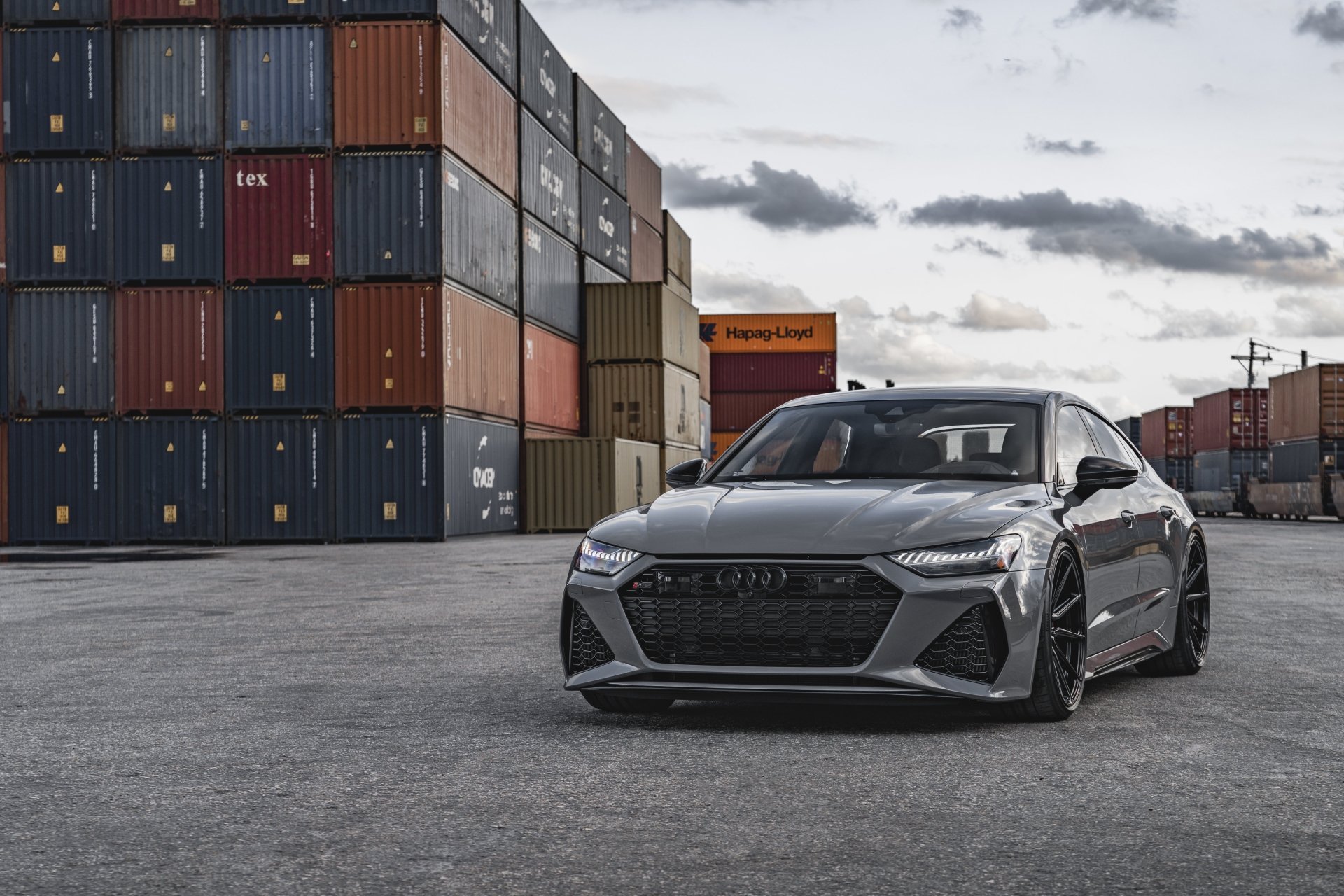 5K Ultra HD PC desktop wallpaper and background: sleek gray Audi RS7 parked in an industrial shipping-container yard under a cloudy sky.