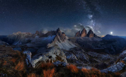 HD wallpaper of the Dolomites under a starry night sky, featuring rugged mountain peaks and the Milky Way illuminating the natural landscape.