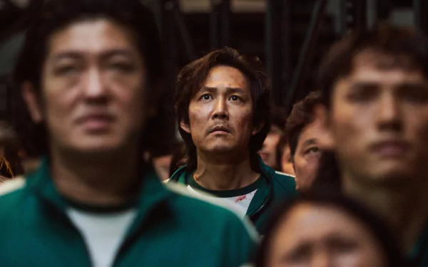 Close-up of a man in a green tracksuit among a tense crowd, scene from the TV show Squid Game, rendered as a 4K Ultra HD PC desktop wallpaper and background.