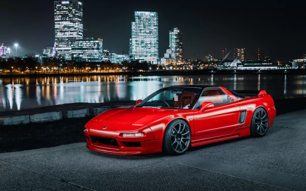 A vibrant red Honda NSX parked by a waterfront at night with illuminated city skyscrapers reflected in the water, captured in 4K Ultra HD for PC desktop wallpaper.