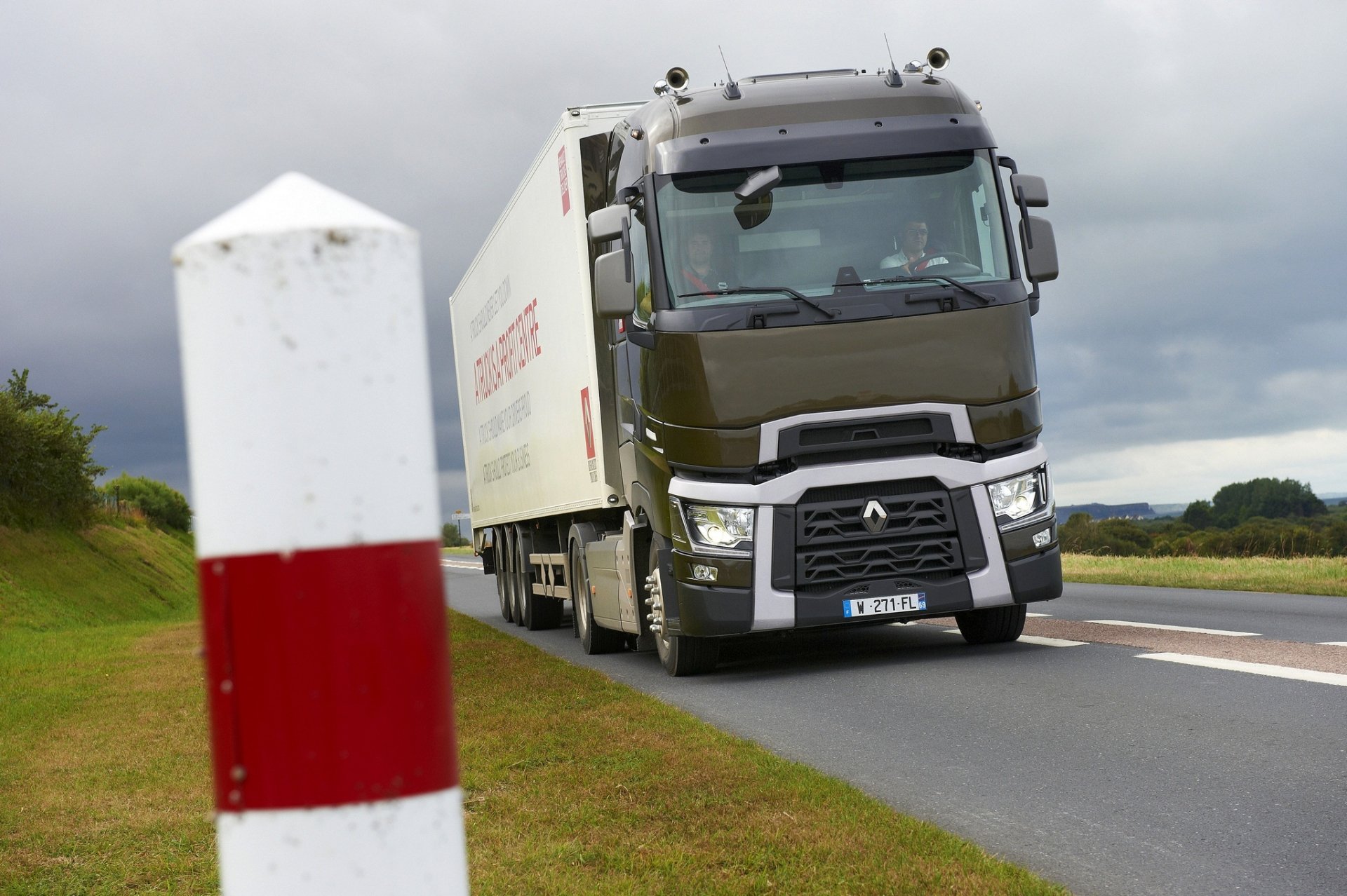 HD PC desktop wallpaper showing a Renault Trucks vehicle — a green semi on a country road with a red-and-white roadside marker and cloudy sky background.