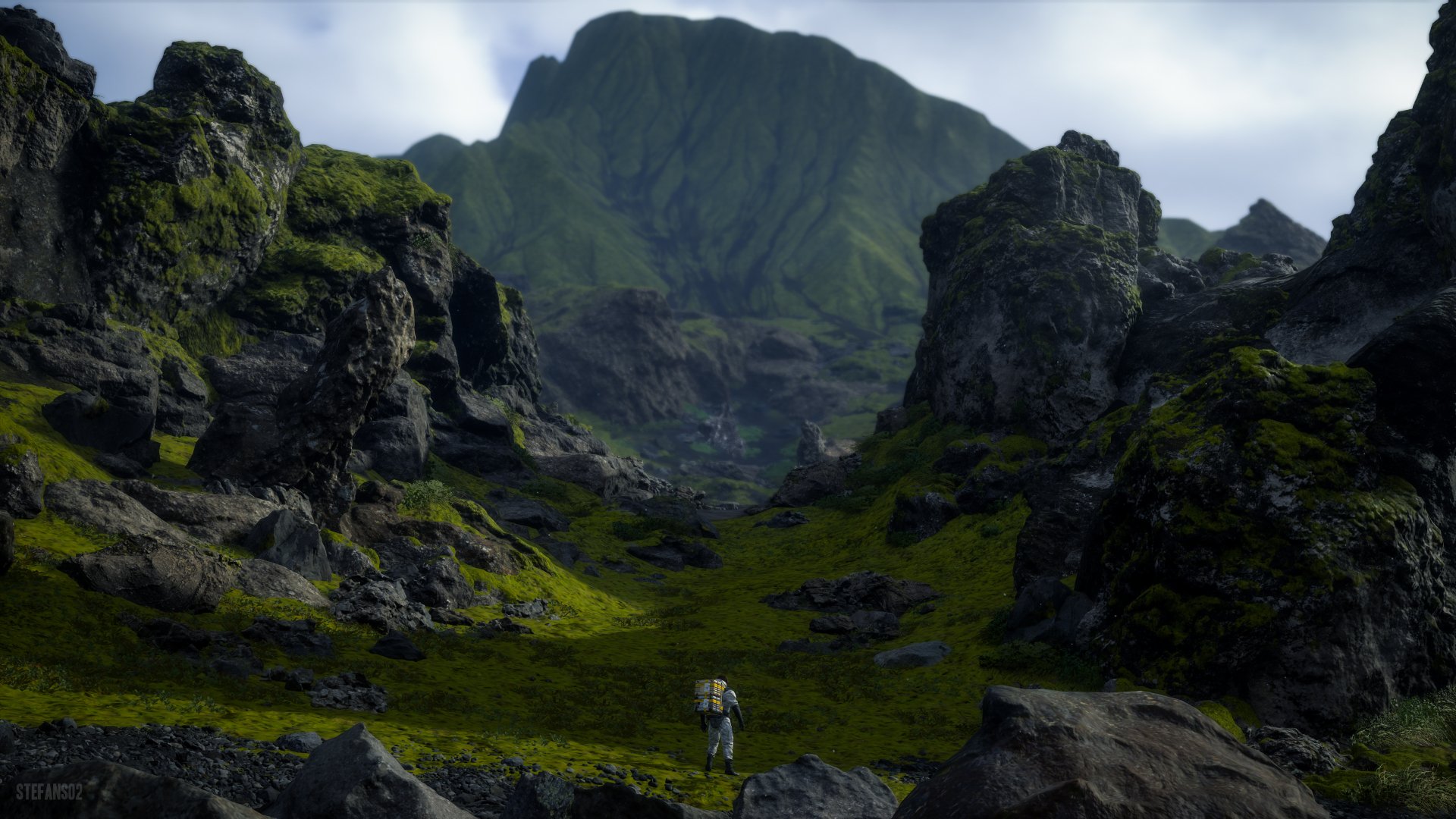 4K Ultra HD Death Stranding video game PC desktop wallpaper: lone porter traverses a mossy, rocky valley toward a mist‑shrouded mountain under a cloudy sky.