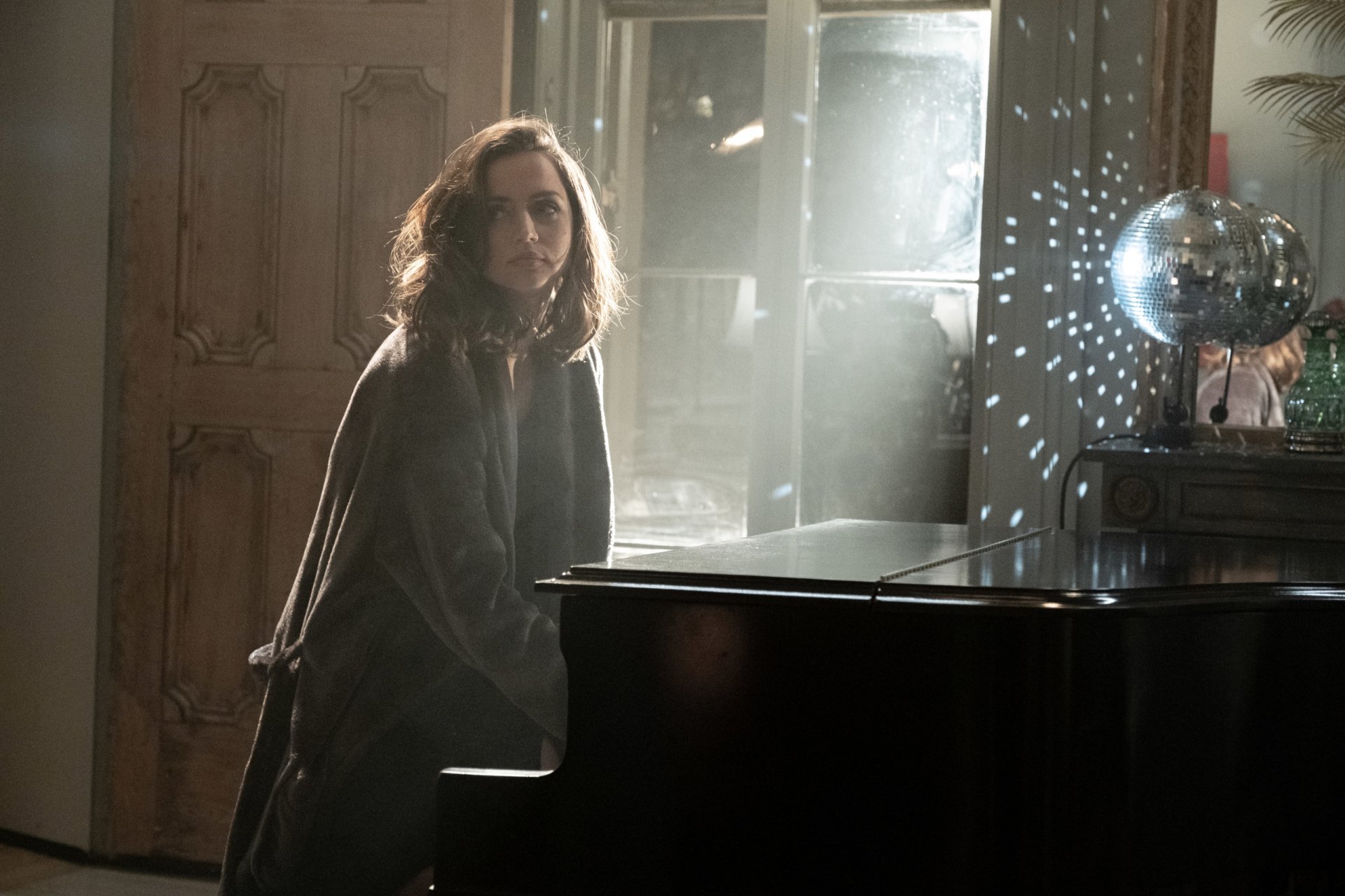 Moody film still from Deep Water: a woman seated at a grand piano in dim, shafted light with a disco ball — 2K Quad HD PC desktop wallpaper/background.