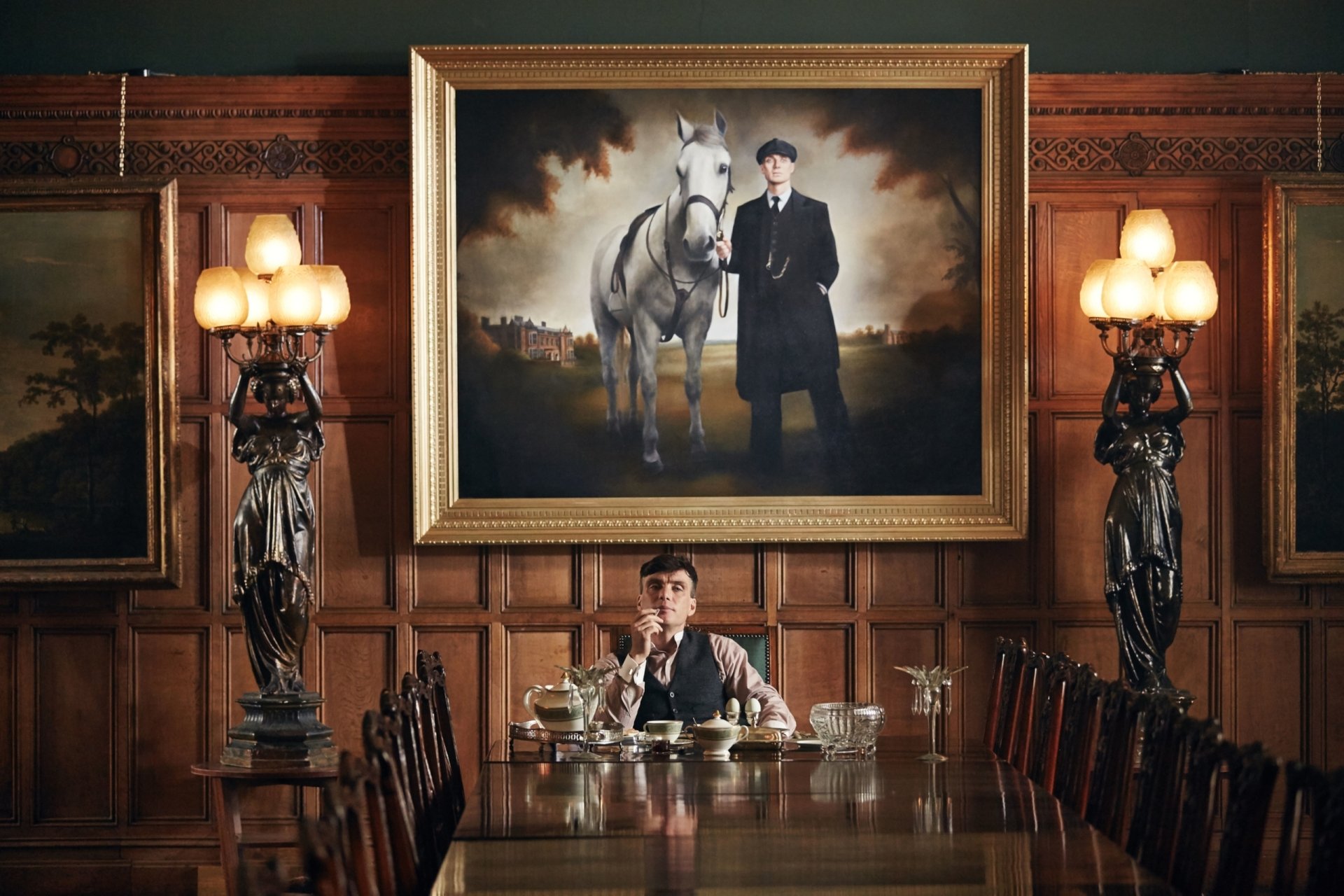 HD desktop wallpaper featuring Cillian Murphy as Thomas Shelby from the TV show Peaky Blinders, seated at a long wooden dining table beneath a large portrait.