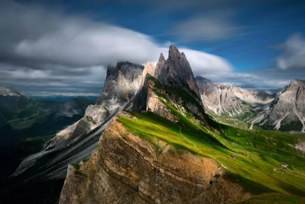 Stunning HD desktop wallpaper of Italy’s Dolomites showcasing rugged mountain peaks and lush green slopes under a dramatic sky.