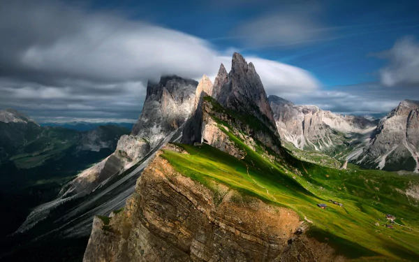 Stunning HD desktop wallpaper of Italy’s Dolomites showcasing rugged mountain peaks and lush green slopes under a dramatic sky.