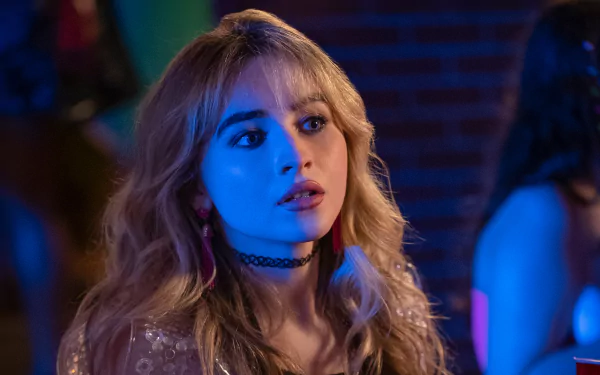 2K Quad HD PC desktop wallpaper for the movie Emergency! — blonde actress under blue club lighting, wearing a choker and glittery top, looking surprised.