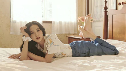 HD PC desktop wallpaper featuring a member of BlackPink lying on a bed in a softly lit room, blending music and serene aesthetics.