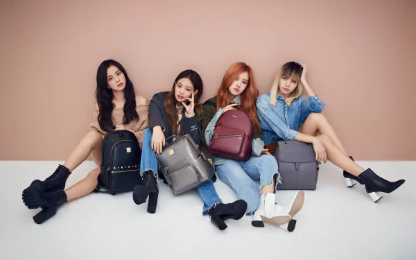 BlackPink members sitting against a peach wall, each holding a stylish backpack, featured in a 4K Ultra HD PC desktop wallpaper celebrating music and fashion.