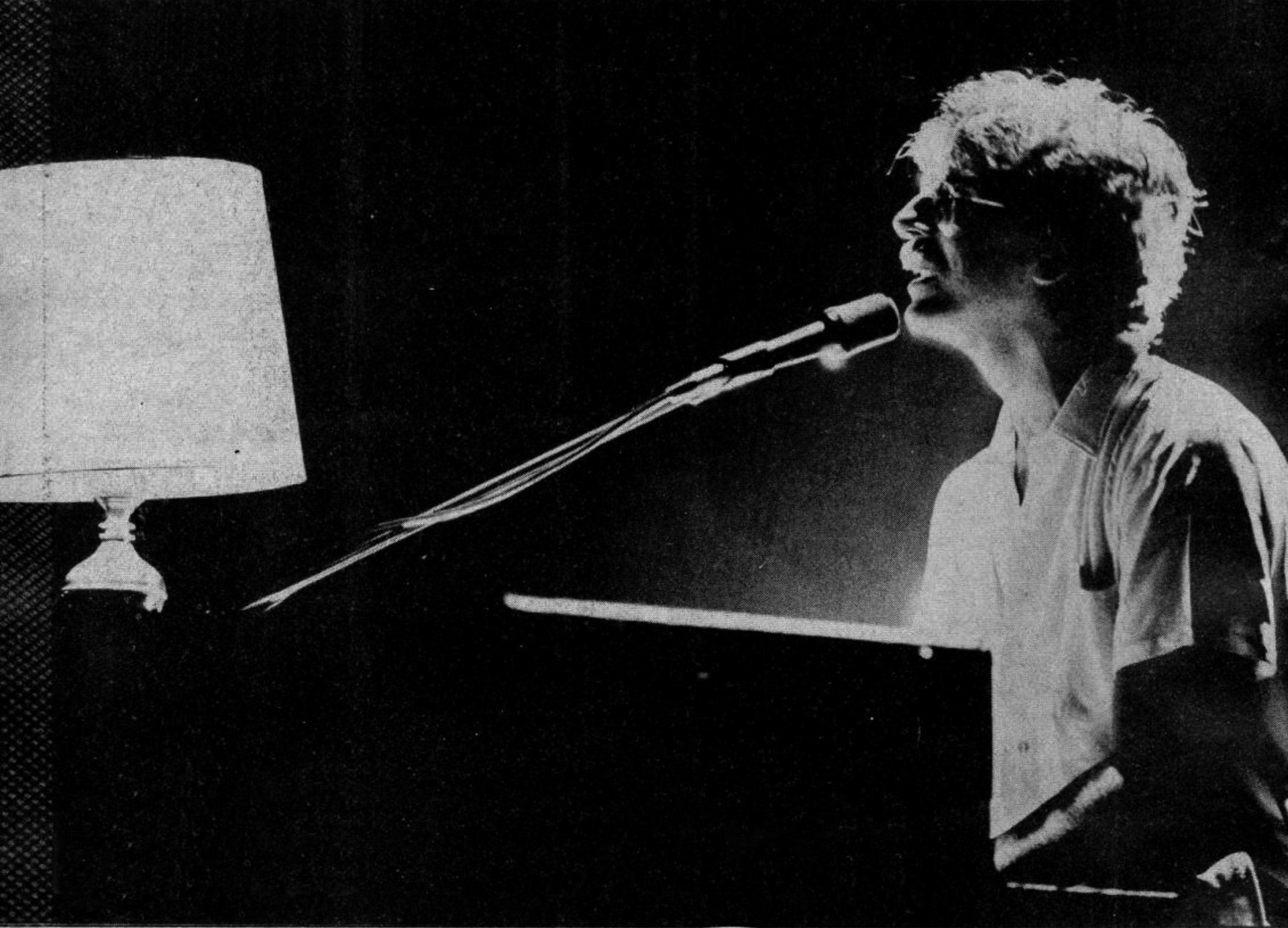 Black-and-white HD PC desktop wallpaper of a pianist singing into a microphone at a piano, illuminated by a nearby lamp and dramatic stage lighting.