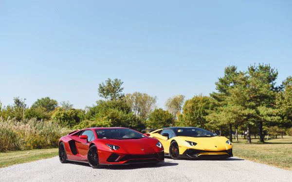 Two Lamborghini Aventador sports cars, red and yellow, parked on a sunlit road by trees — 4K Ultra HD PC desktop wallpaper background.