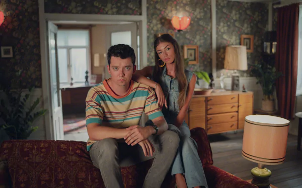 4K Ultra HD PC desktop wallpaper: two young characters seated in a cozy retro living room with warm, moody lighting — TV show Sex Education.