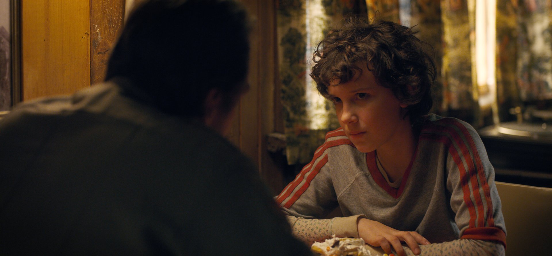 Millie Bobby Brown as Eleven from Stranger Things in a 4K Ultra HD scene, featuring a tense moment from the TV show with detailed indoor lighting and atmosphere.