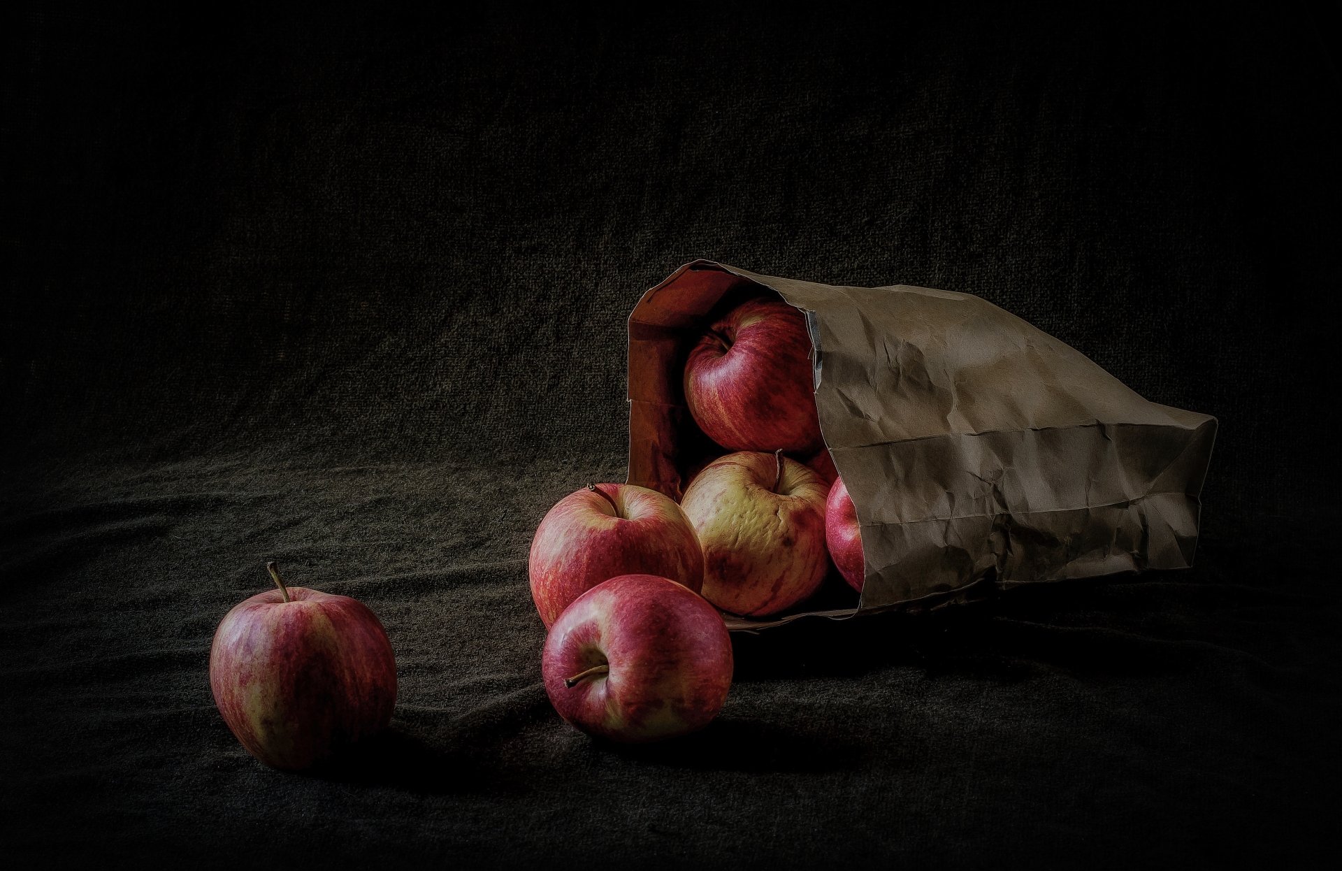 4K Ultra HD PC desktop wallpaper — food: red apples spilling from a crumpled paper bag on a moody, dark textured background.