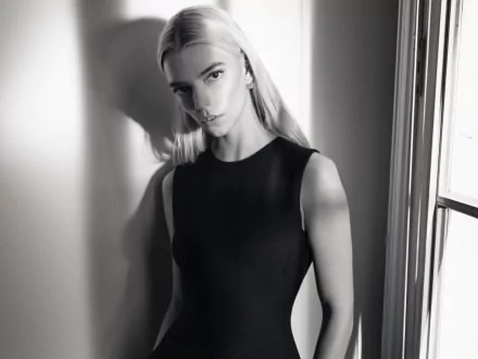 Black-and-white HD PC desktop wallpaper of a blonde female celebrity in a sleeveless black dress, posed by a window with soft shadows and a direct, poised gaze.