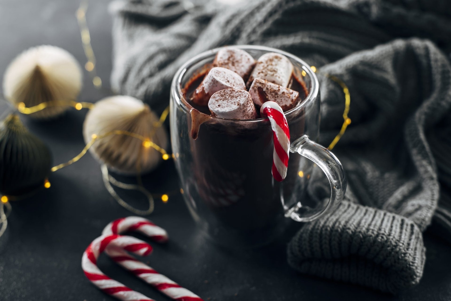 HD PC desktop wallpaper of food: cozy mug of hot chocolate topped with marshmallows, candy cane stirrer, twinkling lights and a knit sweater background.