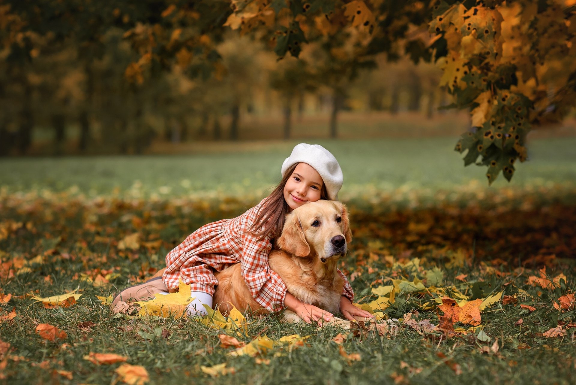 A child in autumn attire hugs a golden retriever while lying on fallen leaves, captured in an HD desktop wallpaper photography.