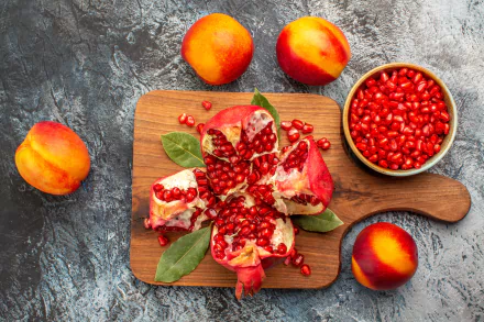 5K Ultra HD PC desktop wallpaper and background: overhead food shot of a split pomegranate with scattered arils on a wooden board, bowl of seeds and ripe peaches on textured slate.