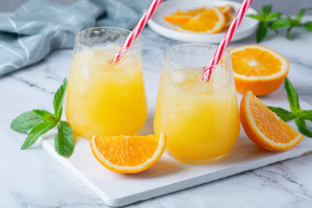 HD PC desktop wallpaper showing food: two glasses of chilled orange juice with ice and red-striped straws, orange wedges and mint on a marble board.