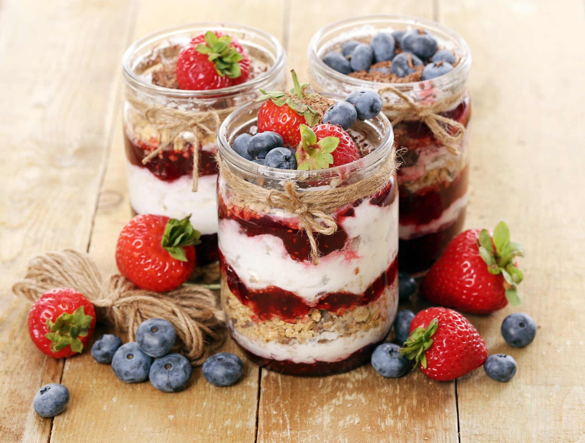 4K Ultra HD PC desktop wallpaper and background showing three layered dessert jars with cream, berry compote and granola, garnished with strawberries and blueberries on a rustic wooden board.