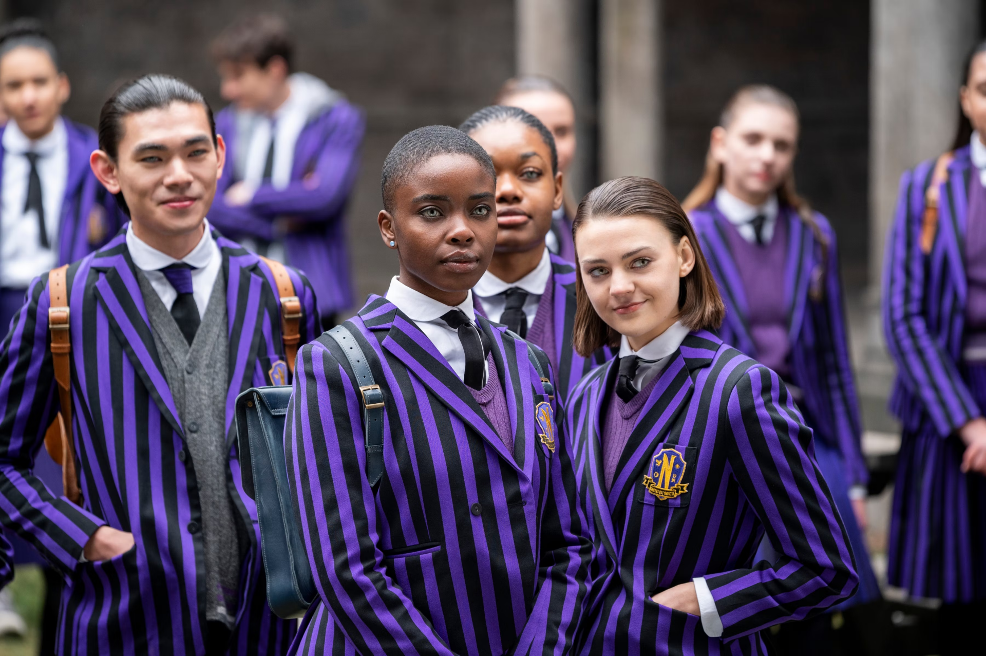 HD PC desktop wallpaper featuring characters from the TV show Wednesday dressed in striking purple and black striped school uniforms outdoors.