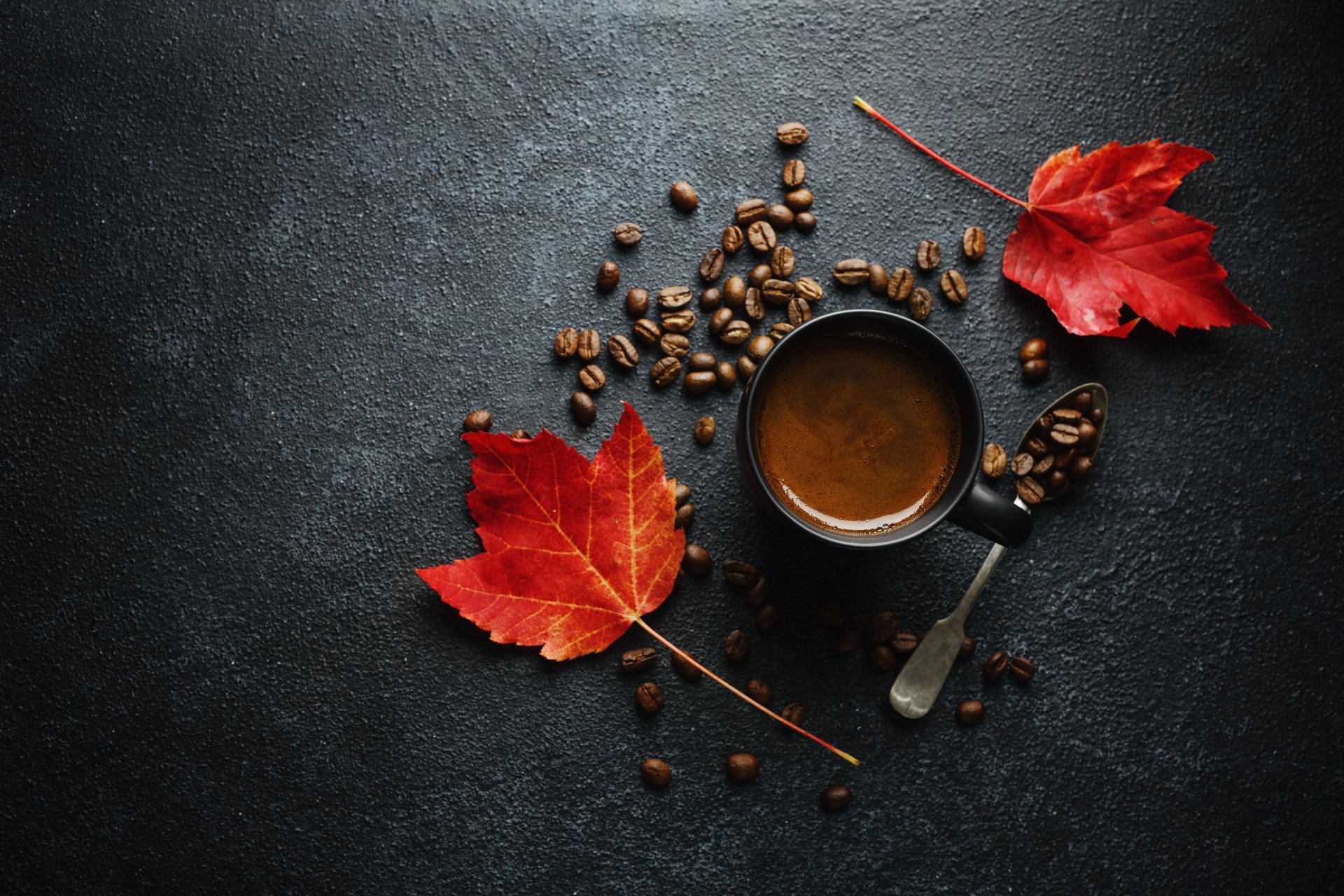 4K Ultra HD desktop wallpaper featuring a cup of coffee surrounded by scattered coffee beans and vibrant red autumn leaves on a dark textured surface.