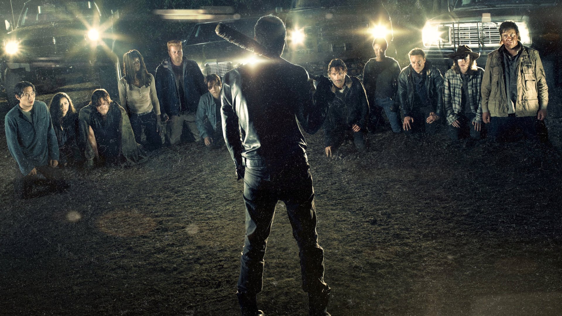 HD desktop wallpaper featuring a tense scene from The Walking Dead TV show with characters gathered in a circle, illuminated by bright lights in a dark setting.