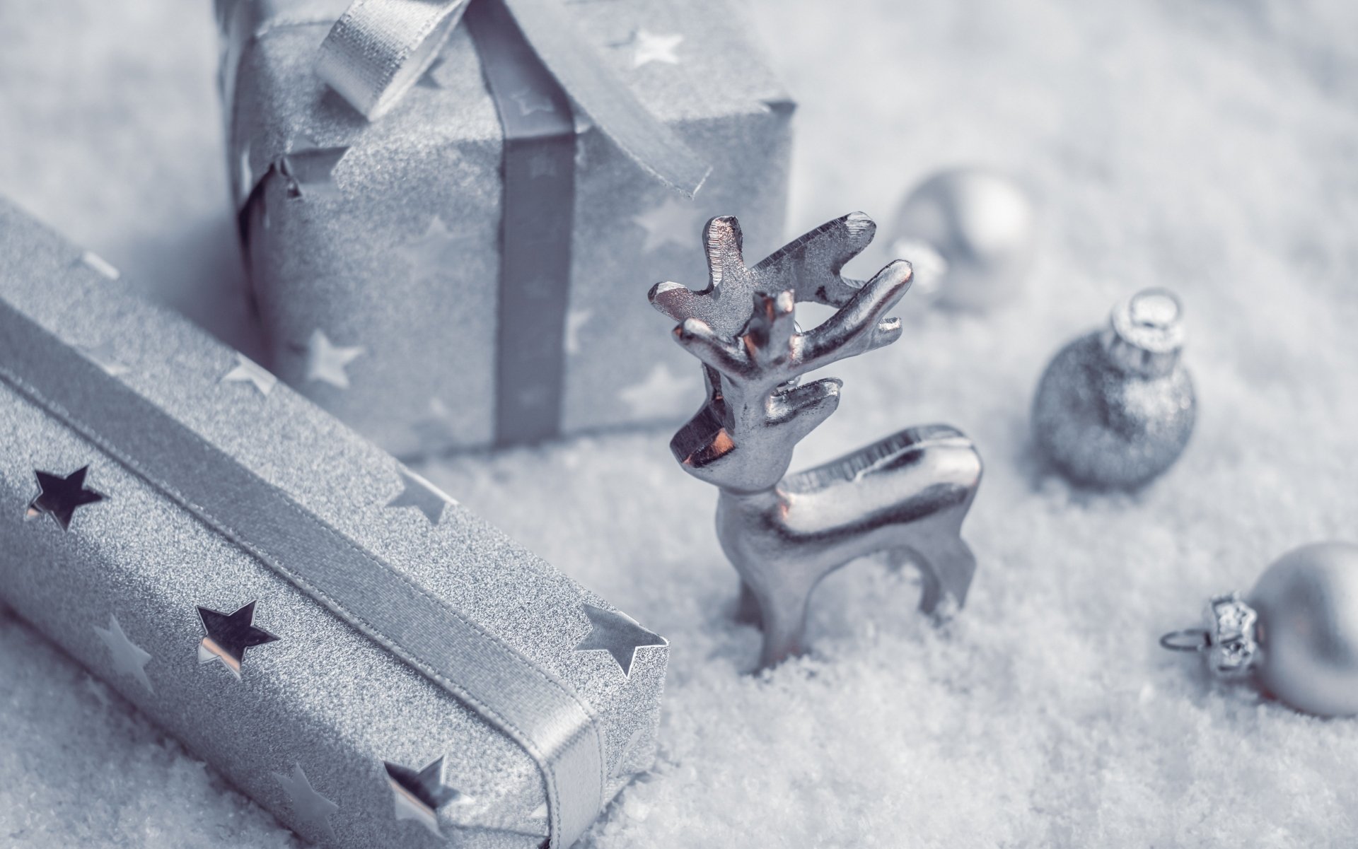 4K Ultra HD Christmas holiday wallpaper featuring silver gift boxes, a small reindeer figurine, and ornaments resting on artificial snow.