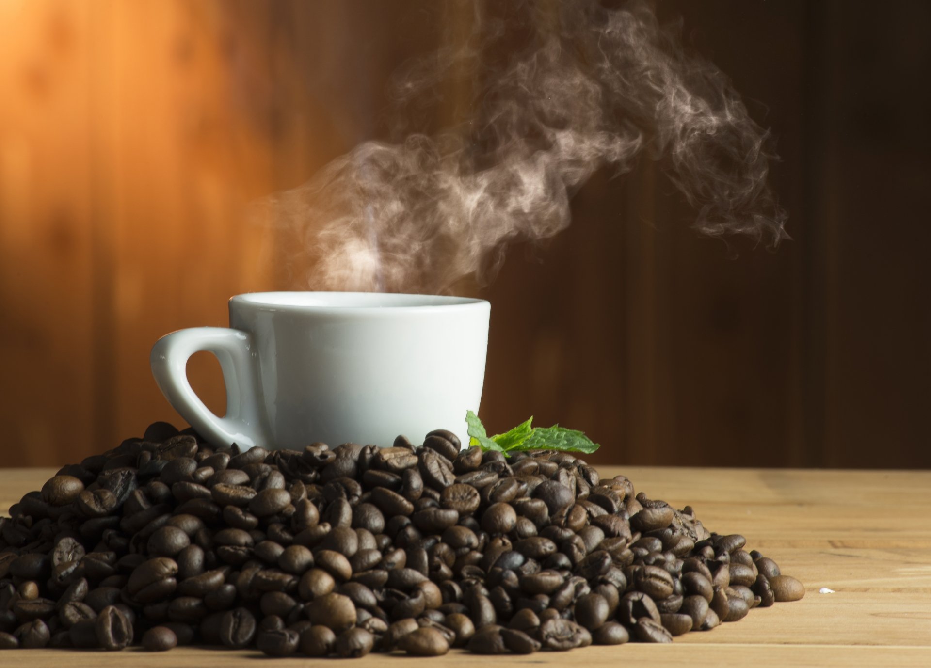 5K Ultra HD PC desktop wallpaper and background — steaming white coffee cup rising from roasted beans on a wooden table, warm brown backdrop (food, coffee).