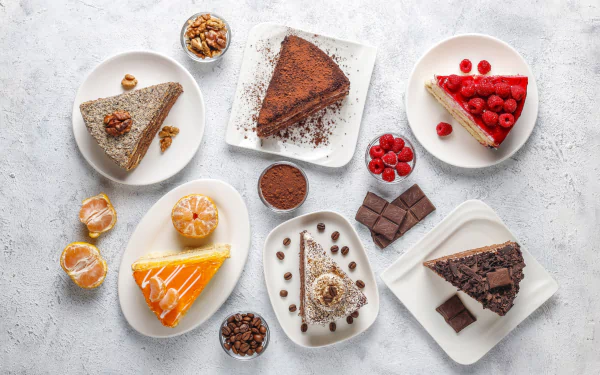 HD desktop wallpaper featuring an assortment of colorful cake slices and chocolate pieces arranged on white plates over a light textured surface.