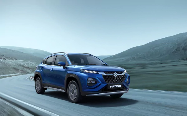 Blue Maruti Suzuki Fronx SUV driving along a winding road with misty hills in the background — 8K Ultra HD PC desktop wallpaper