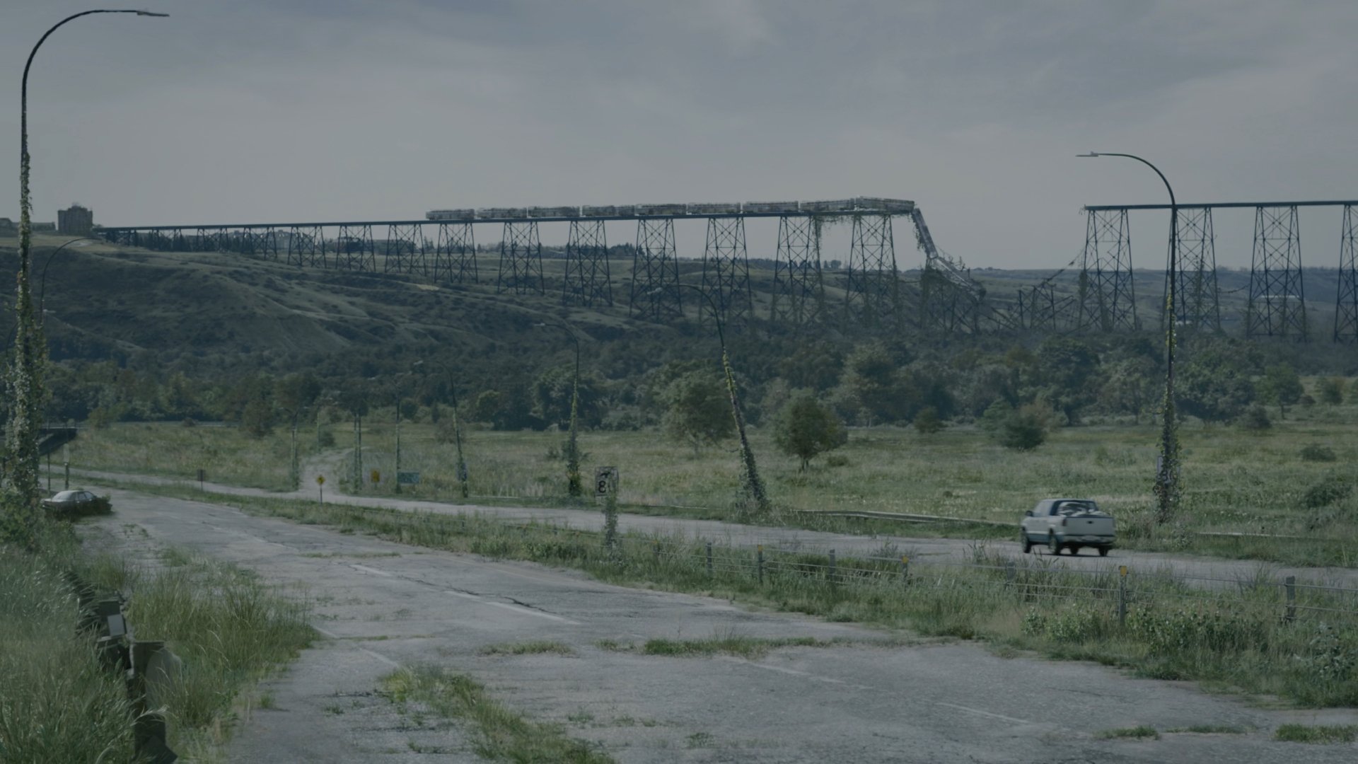 4K Ultra HD PC desktop wallpaper and background from the TV show The Last Of Us: overgrown highway, lone car, sagging power towers beneath a gray sky.