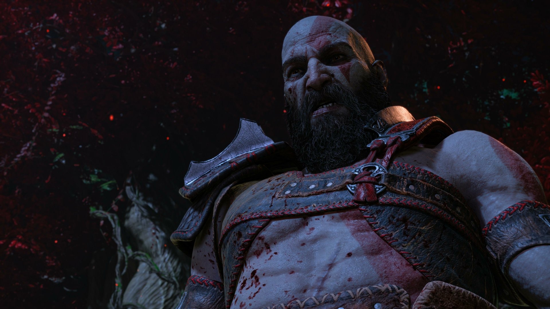 Kratos from God of War: Ragnarök, blood-splattered and battle-worn with a grim expression against a dark wooded backdrop — 4K Ultra HD PC desktop wallpaper.